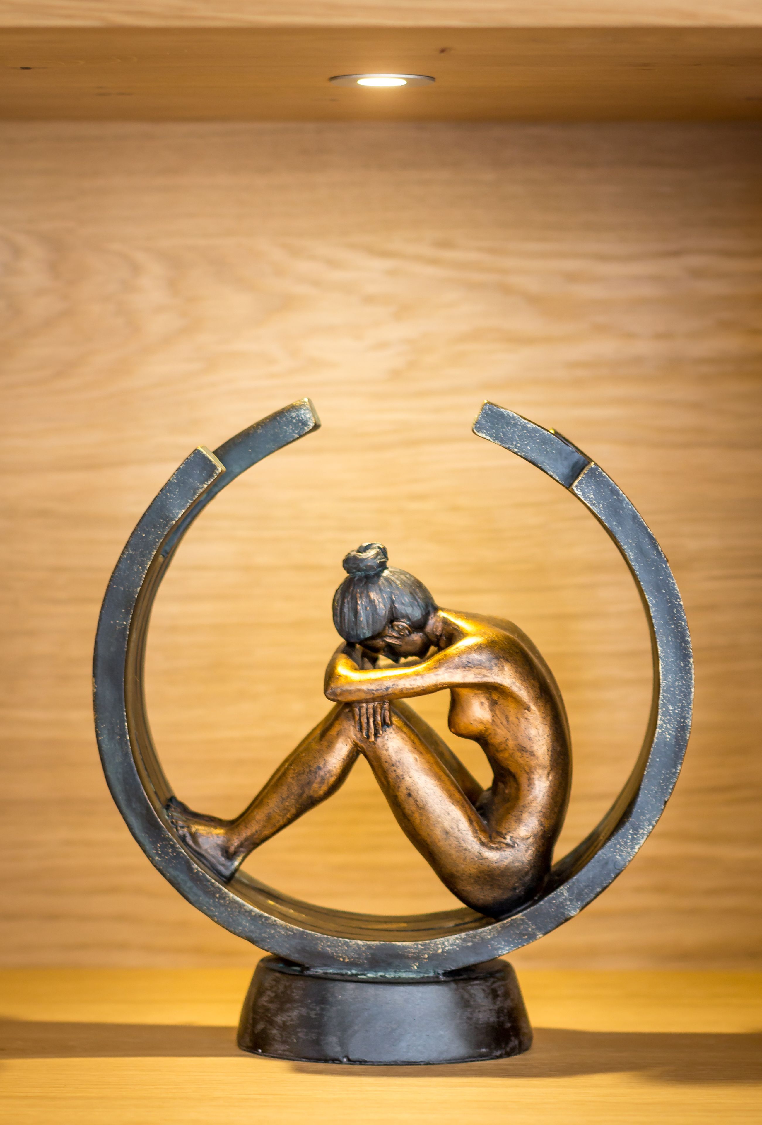 Una escultura de una persona dentro de una estructura metálica curvada.