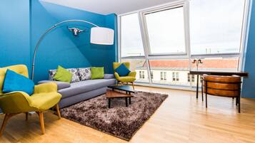 A modern living room with a blue accent wall, a sofa, two armchairs, a coffee table, a rug, and a view of buildings through large windows.