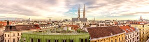 Vista panorámica de un paisaje urbano con destacada arquitectura gótica, incluyendo dos torres gemelas y una catedral, rodeado de edificios urbanos densos.