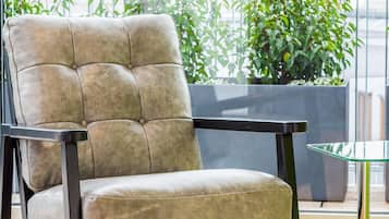 Una silla moderna con asiento y respaldo acolchados, sobre un piso de madera con barandilla metálica y plantas en macetas al fondo.