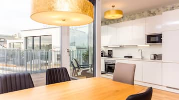 Una cocina moderna con armarios blancos, microondas y estufa. Hay un comedor con una mesa y sillas de madera.