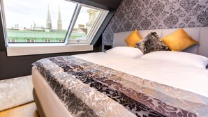 Een slaapkamer met een groot raam, behang met een patroon en een bed met veel kussens.
