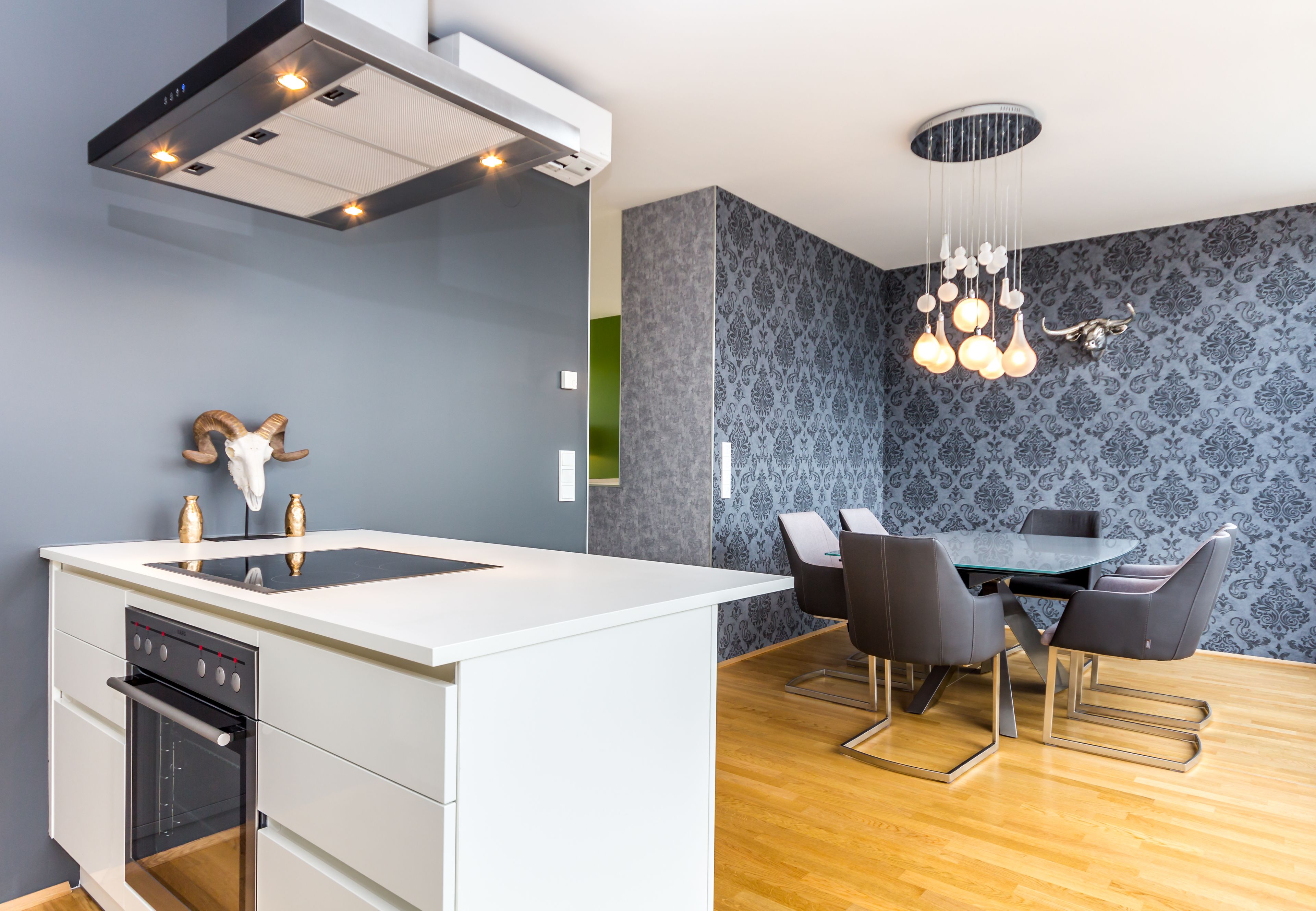 Una cocina moderna con una isla central, horno empotrado y comedor con mesa de vidrio y sillas.