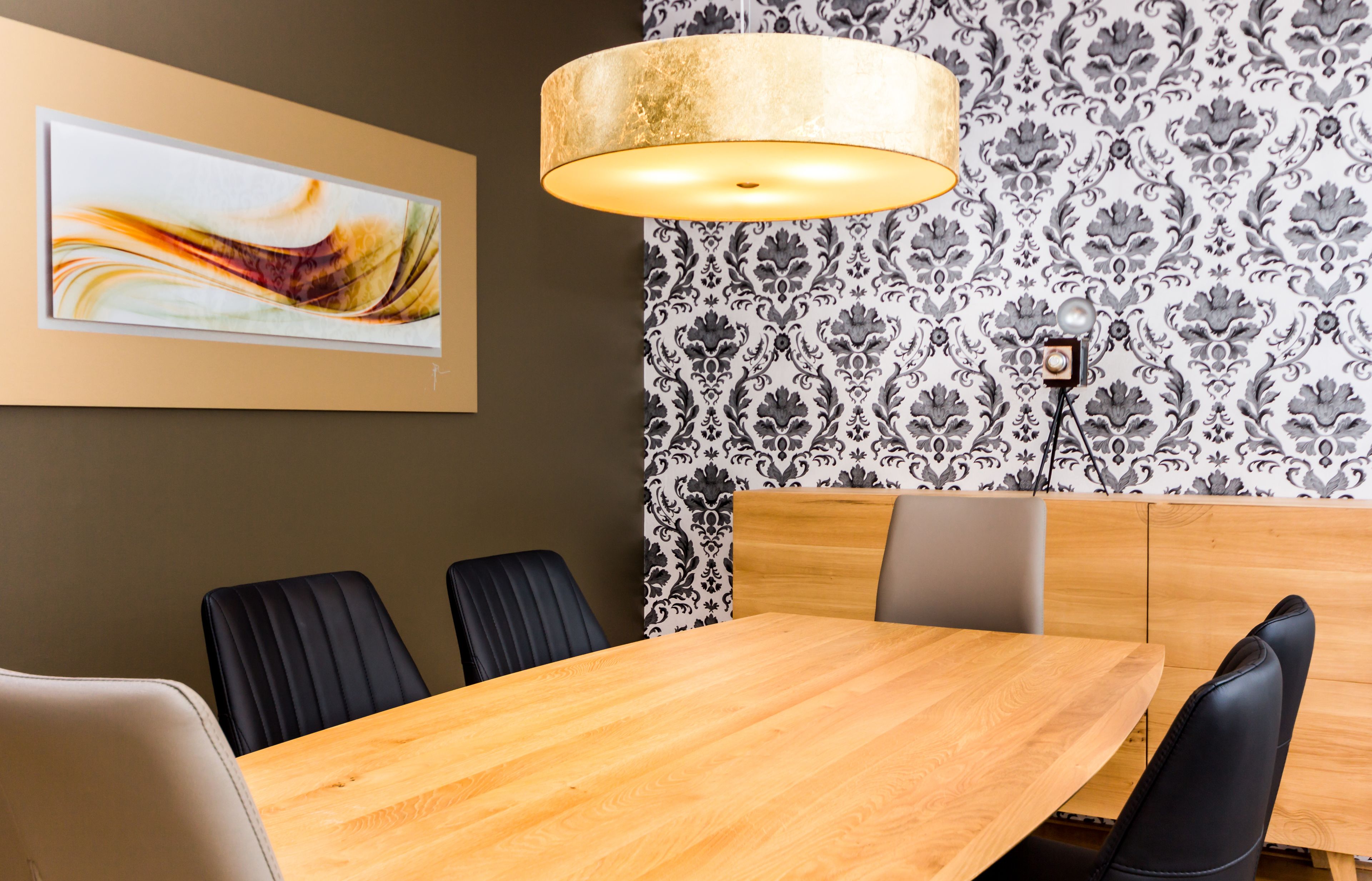 Een congrescentrum met een houten tafel, zwarte stoelen, behang met een patroon en een moderne hanglamp.