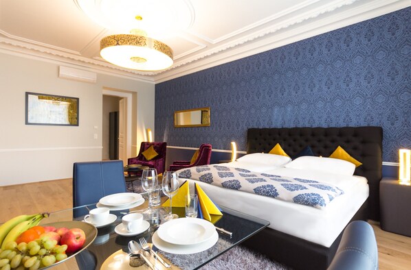 Una habitación de hotel con una mesa de comedor bien organizada, una cama con cabecera capitonada y una pared con estampado azul.