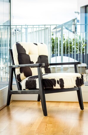 Una silla moderna con estampado blanco y negro, ubicada en una habitación con piso de madera y un ventanal grande.
