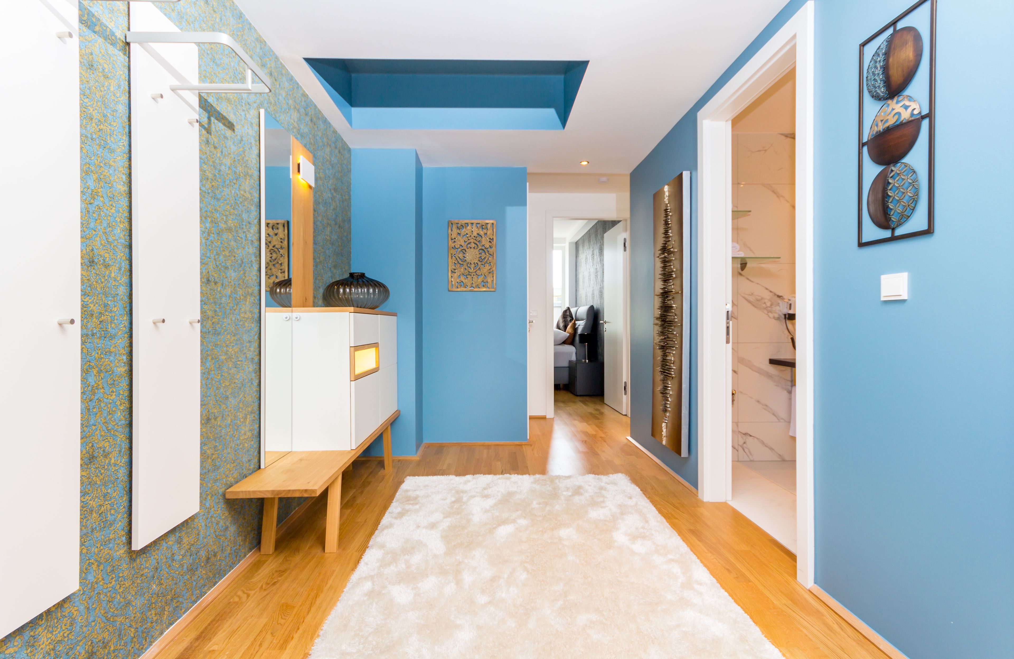 A hallway with a wooden bench, a white console, and a white rug.
