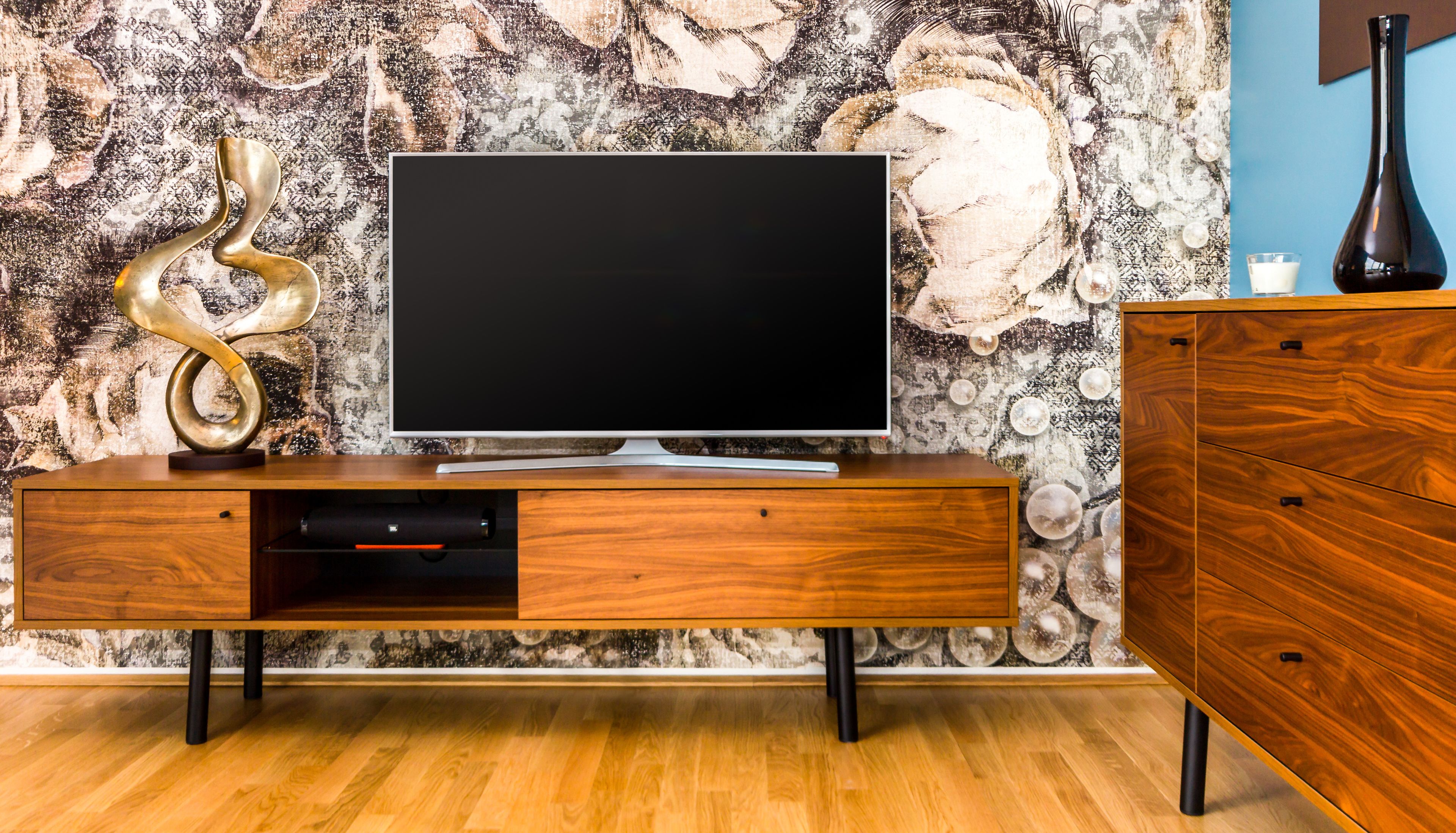 A modern living room with a flat-screen TV on a wooden cabinet, a decorative sculpture, and a wooden dresser.