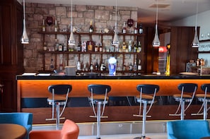 Un espace bar doté d’un comptoir en bois, de tabourets et d’étagères remplies de bouteilles.
