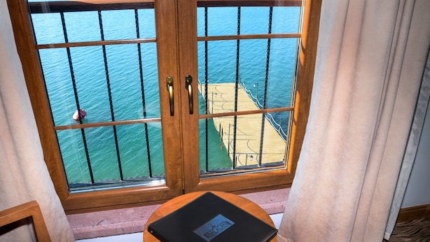 A room with a view of the sea through a window with metal bars, a wooden door, and a small round table with a laptop. - Bacacan Otel (Ayvalik)