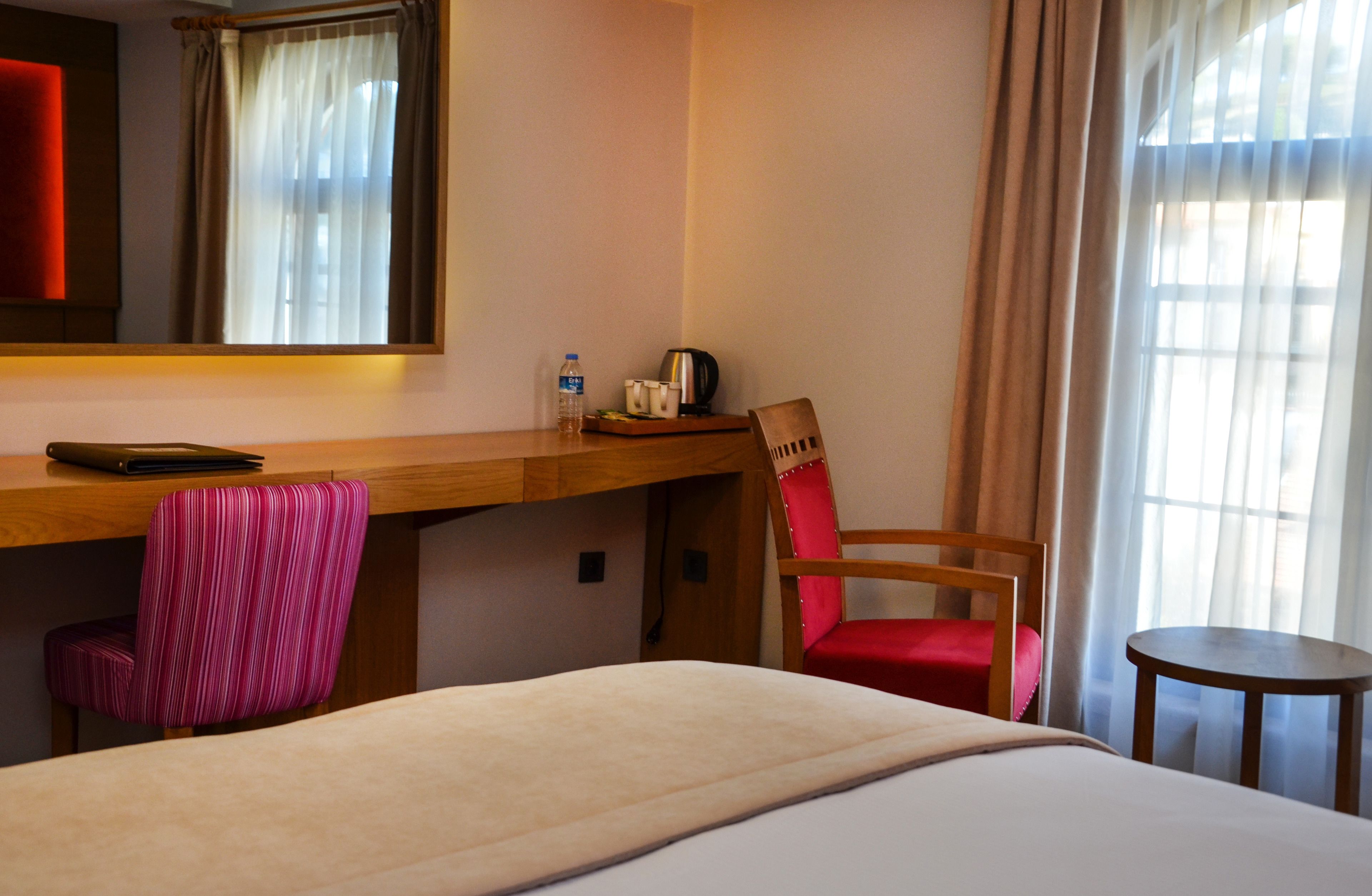 A hotel room with a bed, a desk, a chair, a small table, and a mirror.