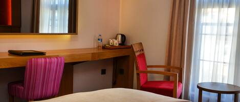 A hotel room with a bed, a desk, a chair, a small table, and a mirror.