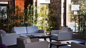 A modern lounge area with sofas and tables, bamboo plants, and a stone wall. - Bacacan Otel (Ayvalik)