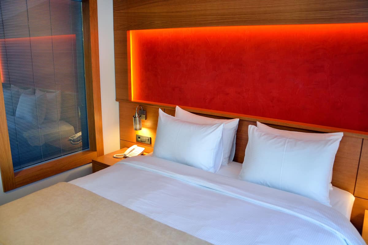 A hotel room with a bed, a nightstand, a telephone, and a window with blinds.