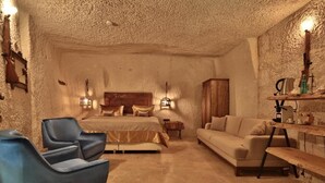 A bedroom with a bed, two bedside tables, a wooden wardrobe, a blue chair, a beige sofa, and a wooden bench. - The Owl Cave Hotel (Nevsehir)