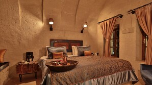 A bedroom with a large bed, a wooden nightstand, a coffee maker, and a tray with fruits and a bottle. - The Owl Cave Hotel (Nevsehir)