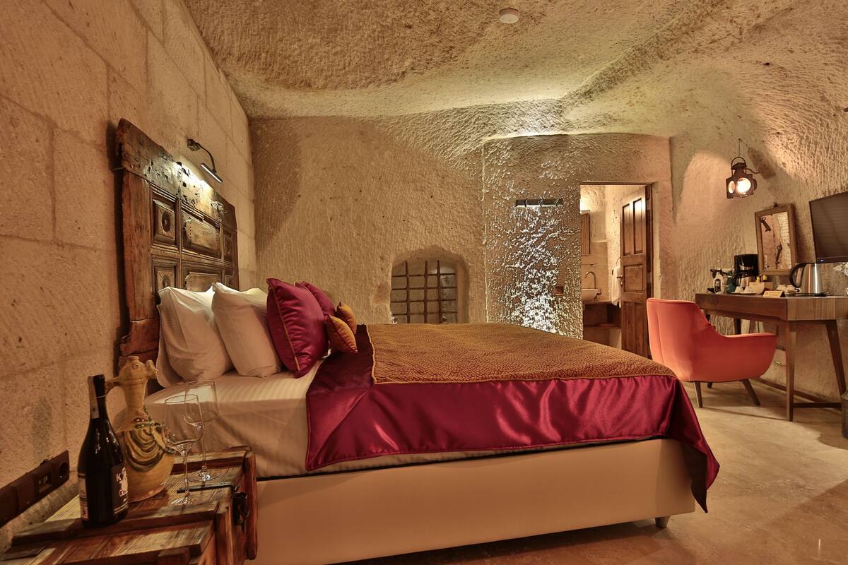 Quarto com cama, escrivaninha, cadeira, garrafa de vinho e um copo.