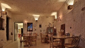 A rustic interior with stone walls, wooden furniture, and a dining area with candles. - The Owl Cave Hotel (Nevsehir)