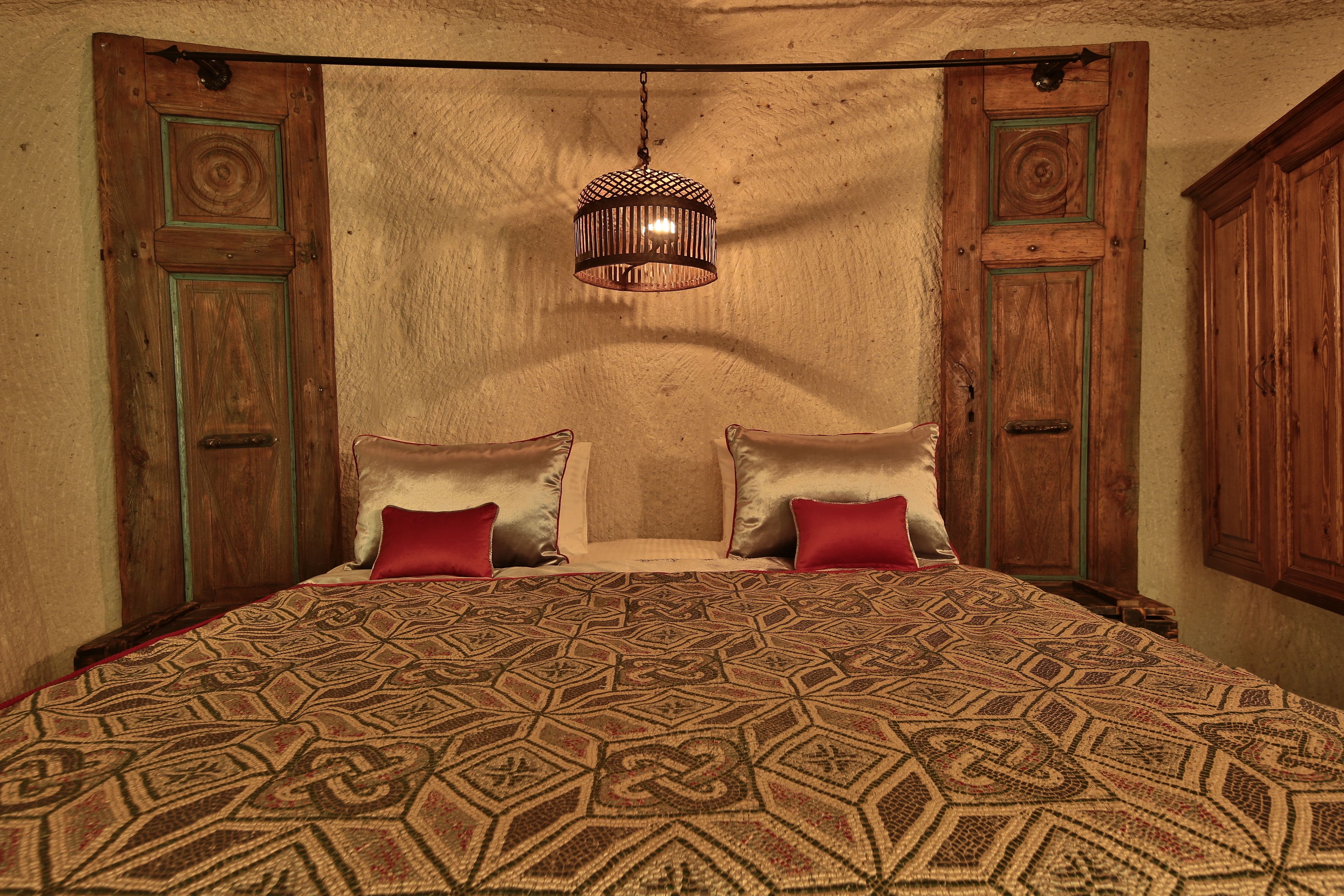 Un dormitorio con una colcha estampada, dos almohadas, una lámpara colgante y puertas de madera.