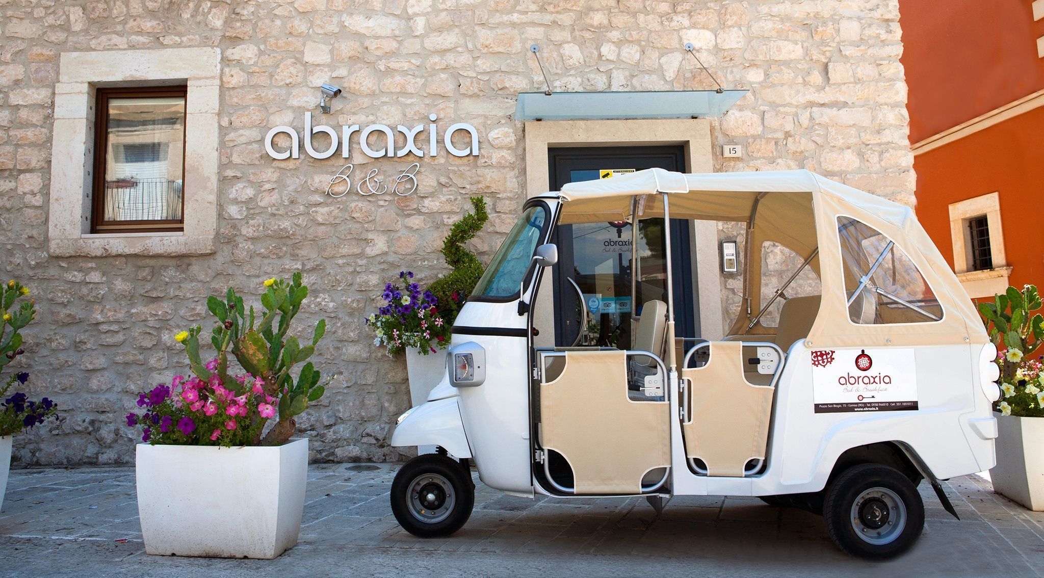 A white three-wheeled vehicle parked in front of a stone building with a sign reading "abraxia".