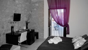 Quarto moderno com parede de pedra, uma mesa com cadeira, cama com toalhas dobradas e janela com cortinas roxas.