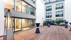Une terrasse intérieure moderne, dotée d’un plancher en bois, d’espaces pour s’asseoir et d’un mur de verre donnant sur un immeuble.