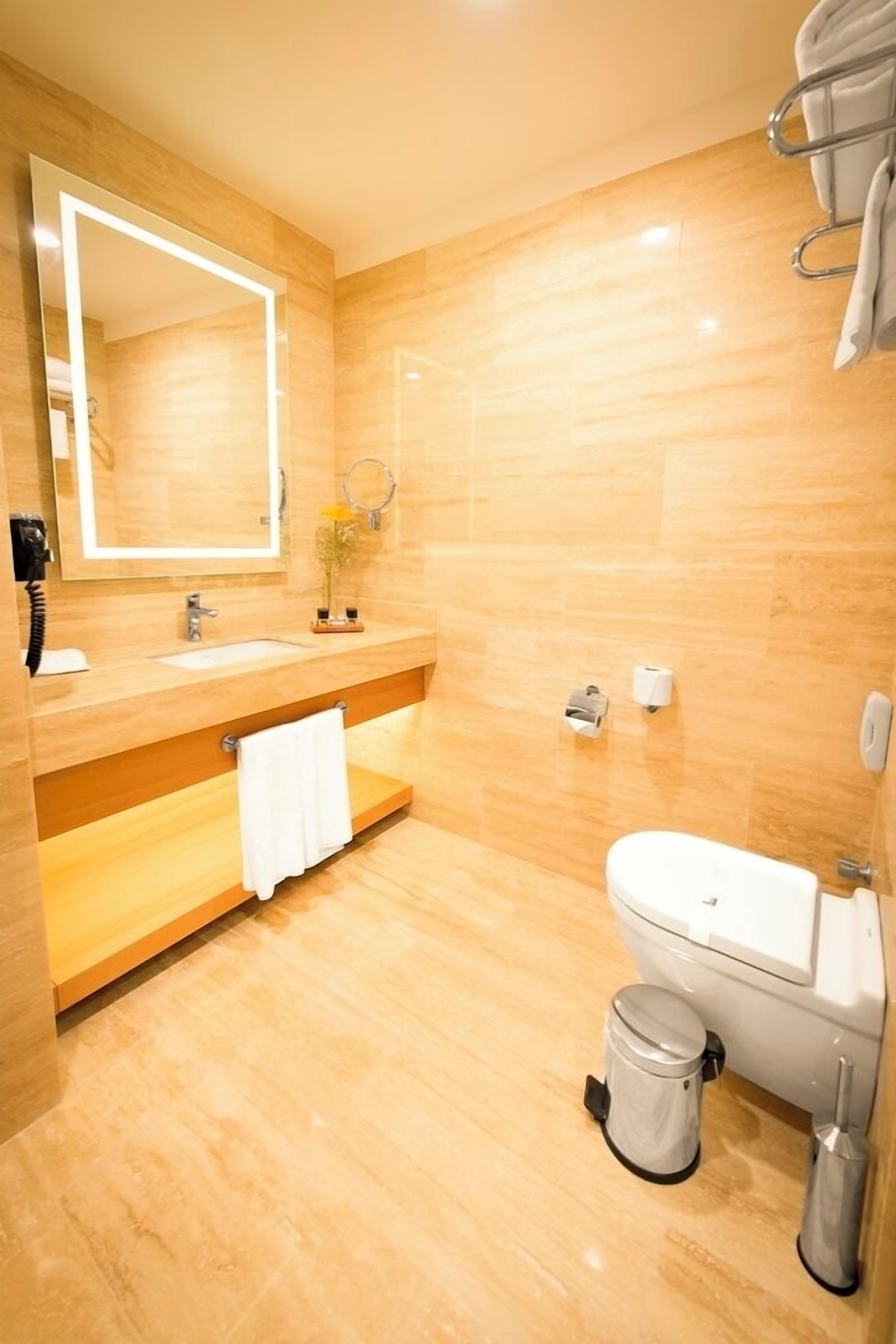 A modern bathroom with a wooden vanity, a large mirror, a toilet, and a trash can.