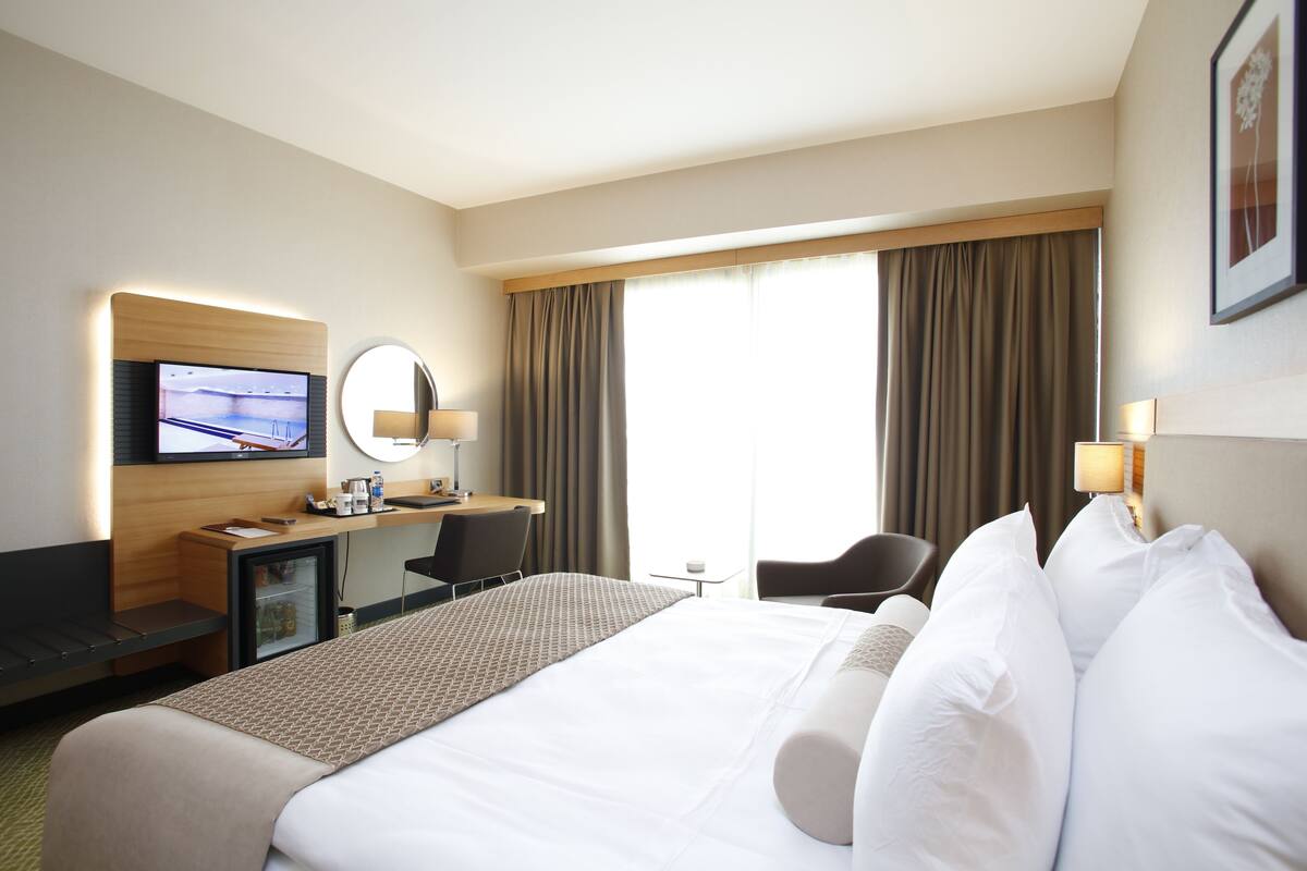 A hotel room with a large bed, a desk with a computer, a TV, and a small table.