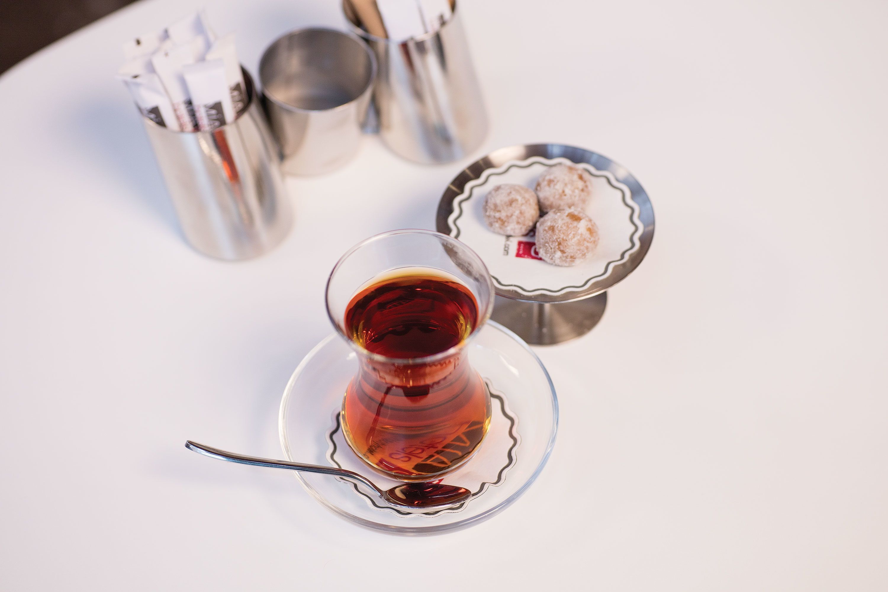 Eine Teetasse auf einem Untertasse mit einem Löffel, eine Metalltasse und ein Teller mit zwei runden Gebäcken.