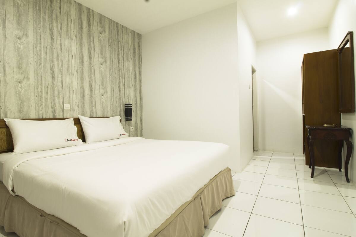 A hotel room with a large bed, a wooden headboard, a wooden wardrobe, and a tiled floor.