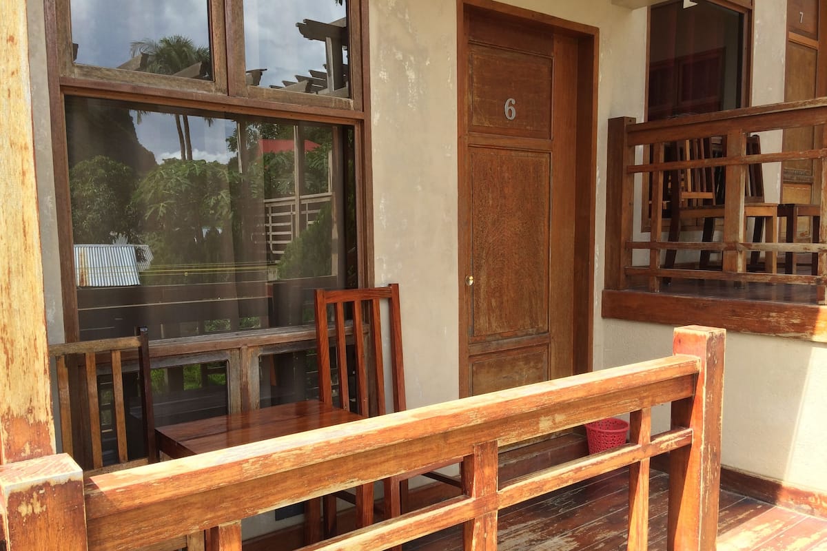 A wooden bench and chair in front of a window with a view of a building and trees.