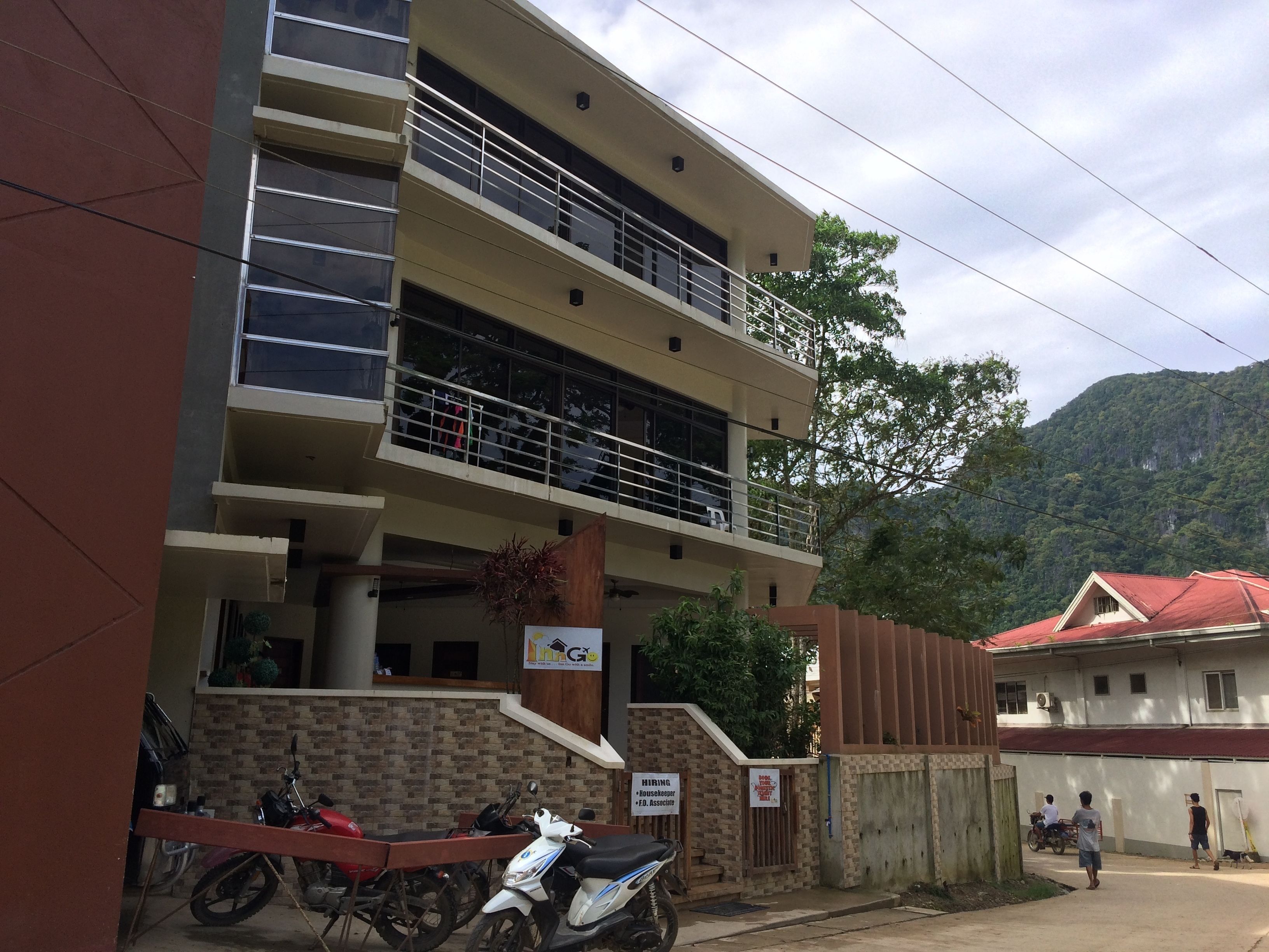 Um edifício com vários andares, uma varanda, um aviso indicando serviços de recrutamento e uma entrada com portão.