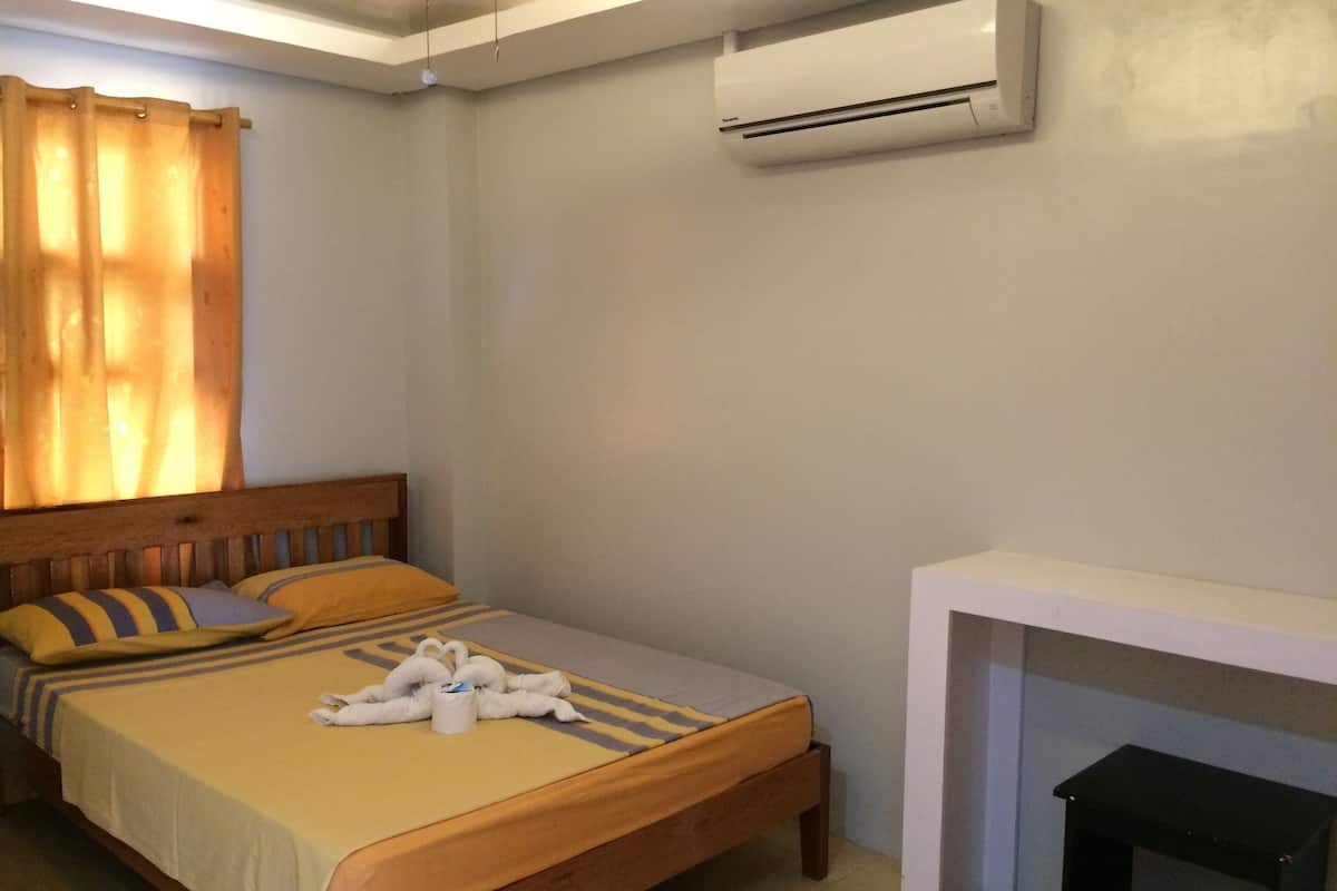A bedroom with a bed, a bedside table, an air conditioner, and a window with curtains.