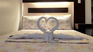 A bed with a floral bedspread, heart-shaped towels, and a bedside table with a lamp. - Inngo Tourist Inn (El Nido)