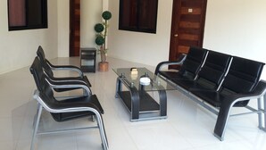 A modern waiting area with a glass table, two black chairs, a small potted plant, and a wooden door. - Inngo Tourist Inn (El Nido)