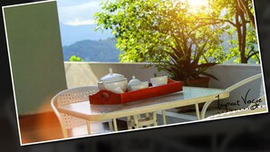 Un balcón con una mesa, una bandeja roja con teteras y tazas, y una planta en maceta.