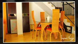 Un área de comedor con sillas de mimbre, una mesa de vidrio, un aparador de madera y una escalera con barandilla negra.