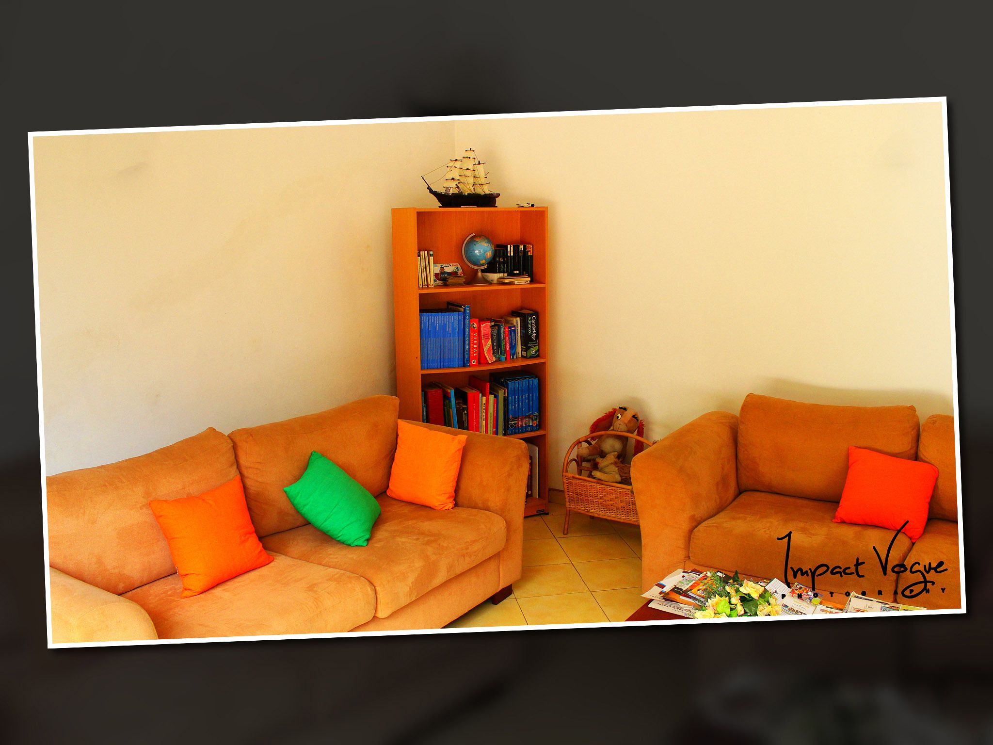 A living room with two orange sofas, a bookshelf, and a small ship model on top.