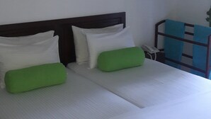 Una cama con ropa de cama blanca, almohadas verdes, un cabecero de madera y una silla azul con una toalla.