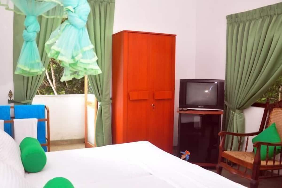 A bedroom with a bed, a wooden wardrobe, a television, and a chair.