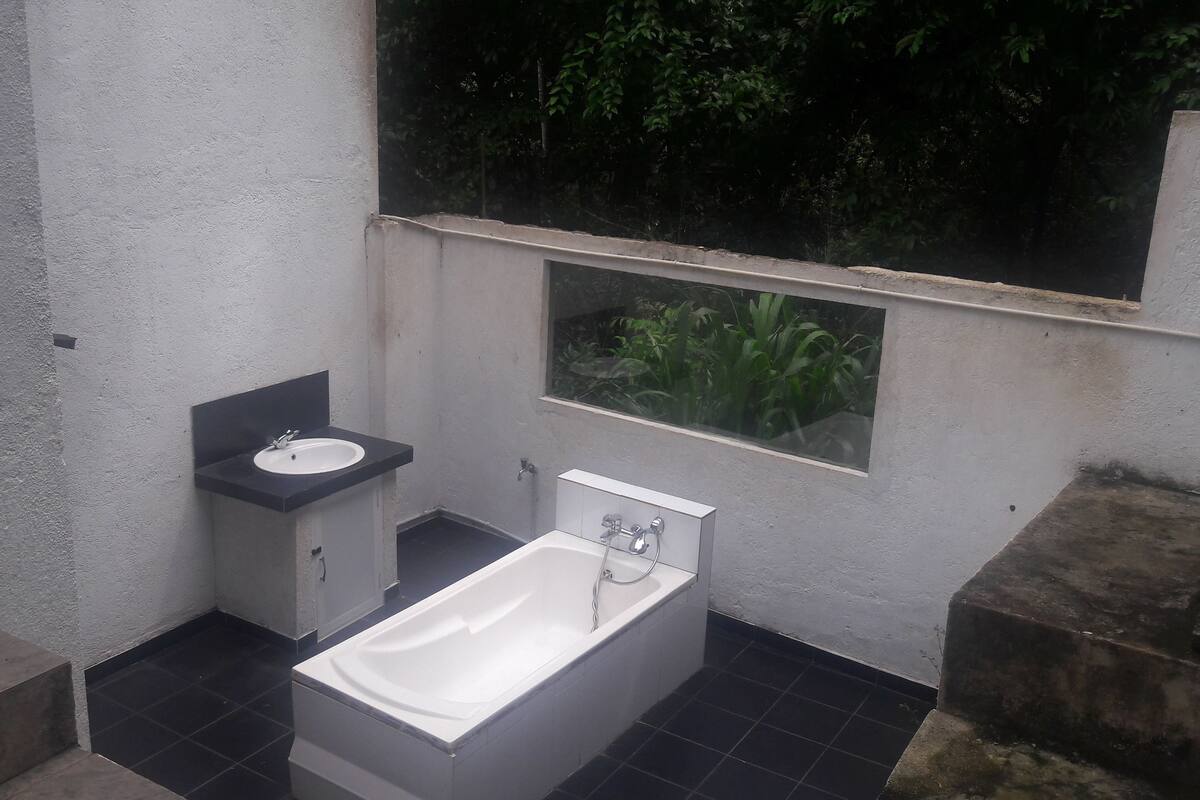 A bathroom with a bathtub, a sink, and a window overlooking greenery.