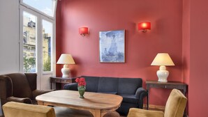 Ein Zimmer mit roter Wand, einem Sofa, zwei Sesseln, einem Holztisch und zwei Lampen.