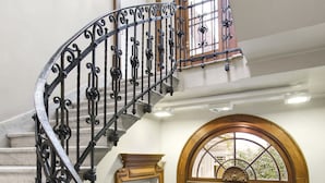 Eine prächtige Wendeltreppe mit aufwendiger schwarzer Eisenbalustrade, die zu einer Empore mit einer großen Holztür und einem Fenster mit dekorativem Glas führt.
