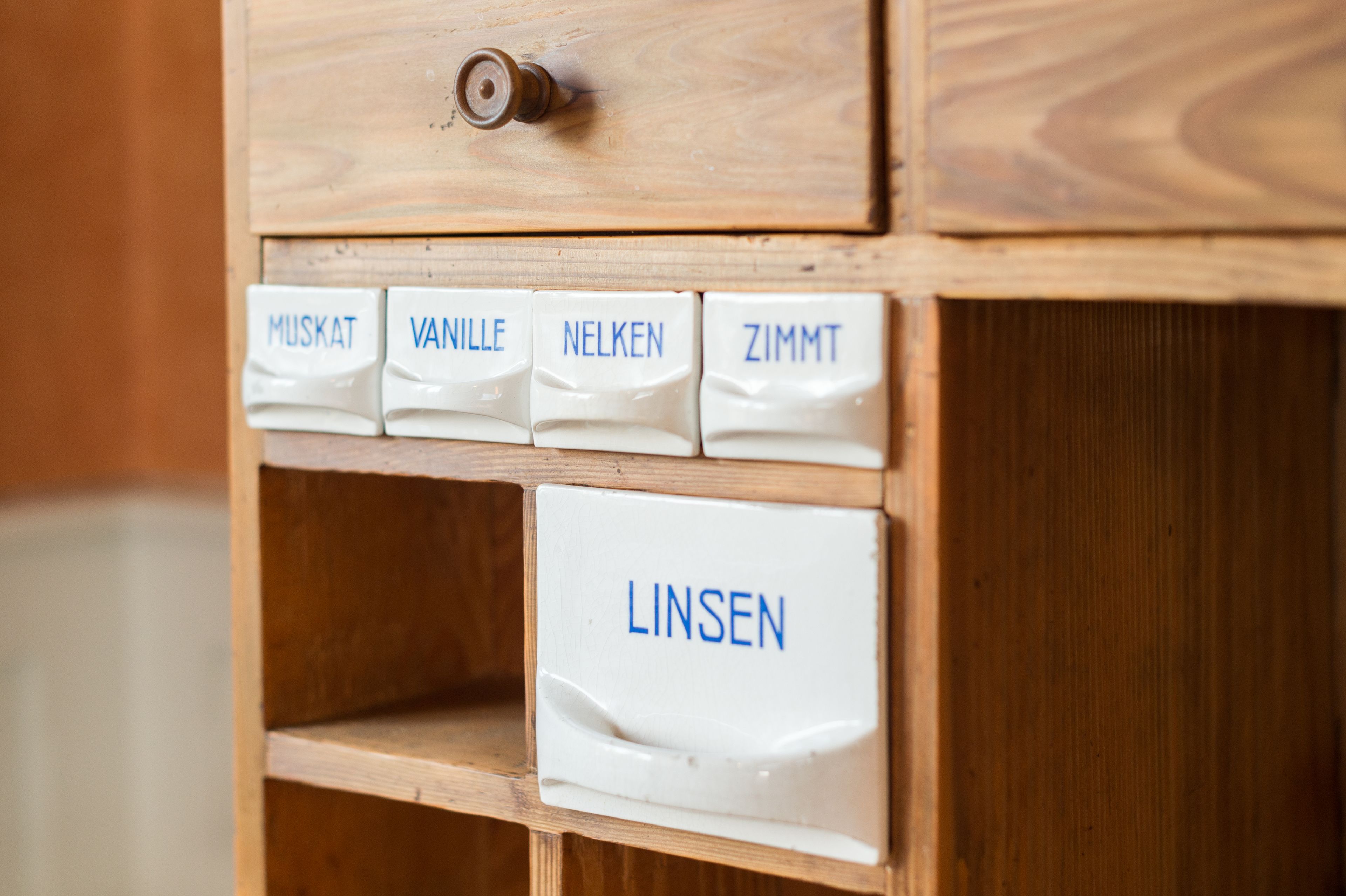 Un armari de fusta amb compartiments etiquetats com a ‘MUSKAT’, ‘VANILLE’, ‘NELKEN’, ‘ZIMMT’ i ‘LINSE’.