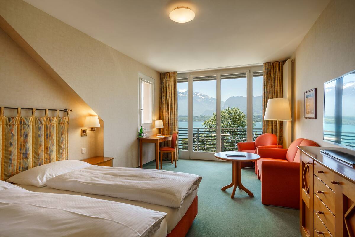 Een hotelkamer met een bed, een bureau, een stoel, een bank en uitzicht op bergen.