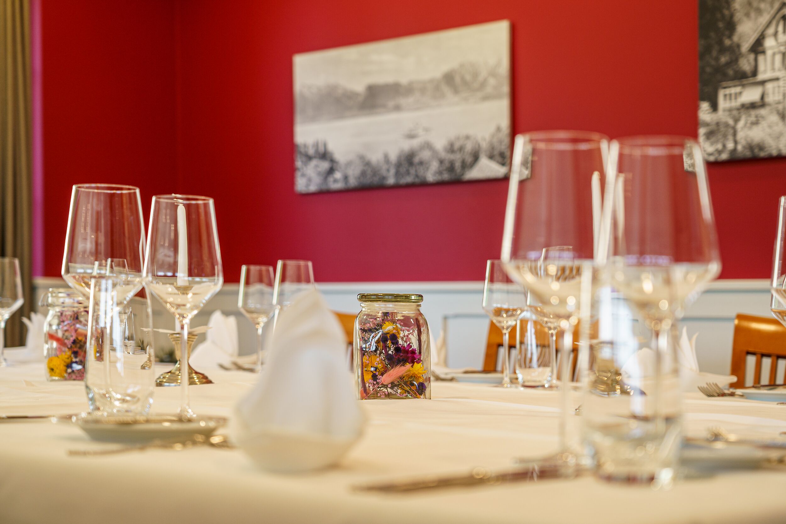 A dining table set with wine glasses, a jar of colorful flowers, and a white napkin.