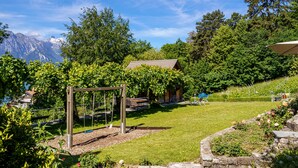 Een tuin met een schommel, een houten constructie en een stenen muur.