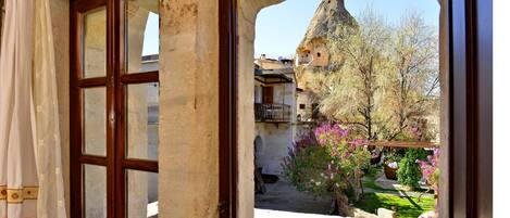 Vista a través de una puerta que da a un patio con un edificio, un árbol y un arbusto de flores.