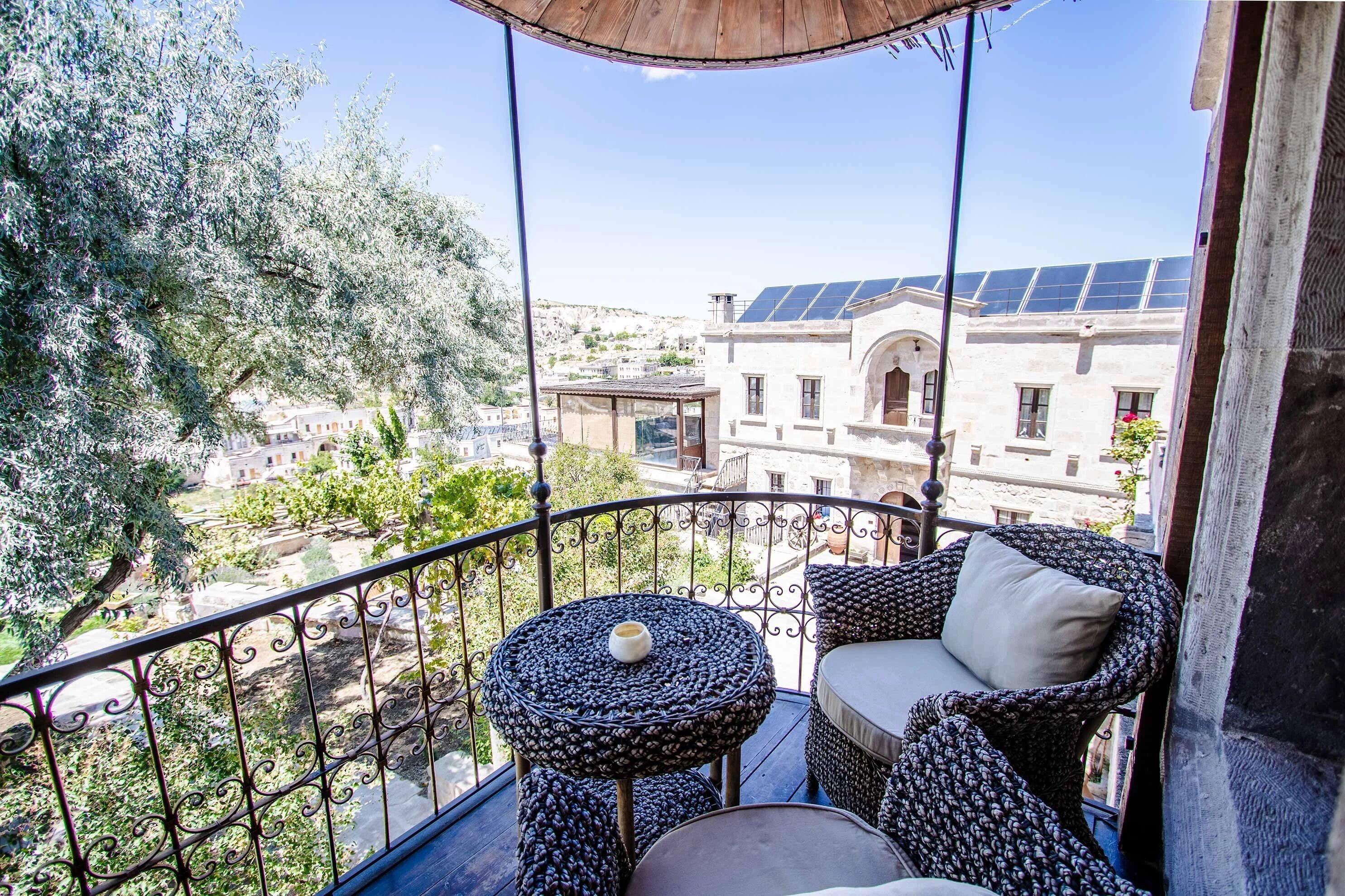 Ein Balkon mit Korbmöbeln, einem kleinen runden Tisch und Blick auf Häuser und Bäume.