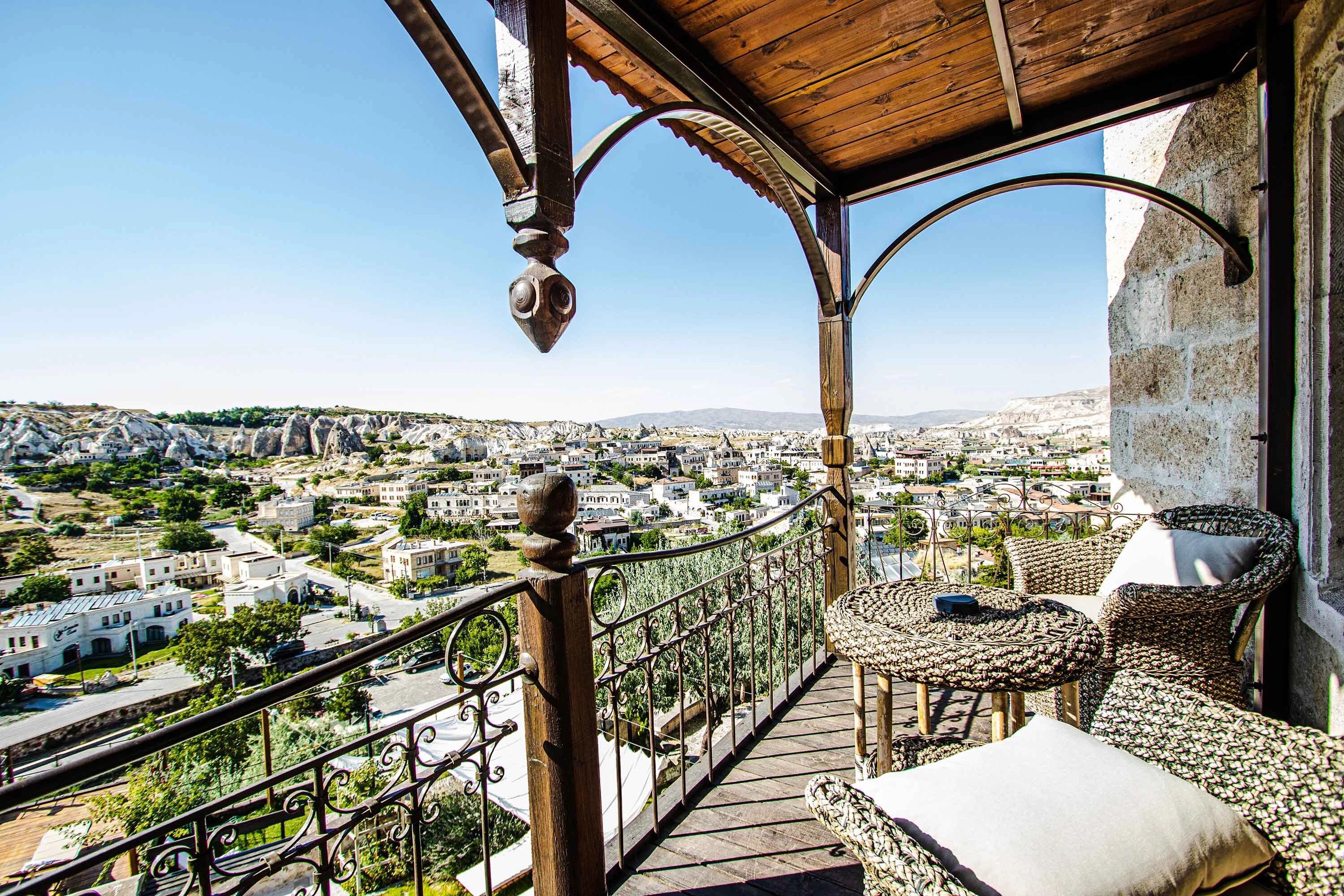 A balcony with a view of a cityscape, featuring a wrought iron railing and wicker furniture.